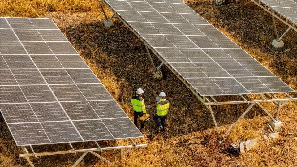 Photovoltaik-Farm von oben, Ingenieure gehen zwischen den Modulen