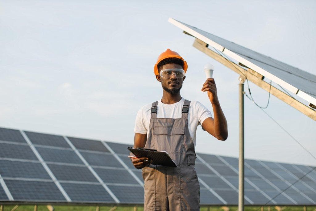 Mann steht auf Solarfarm und hält eine Glühbirne als Symbol für Solarenergie