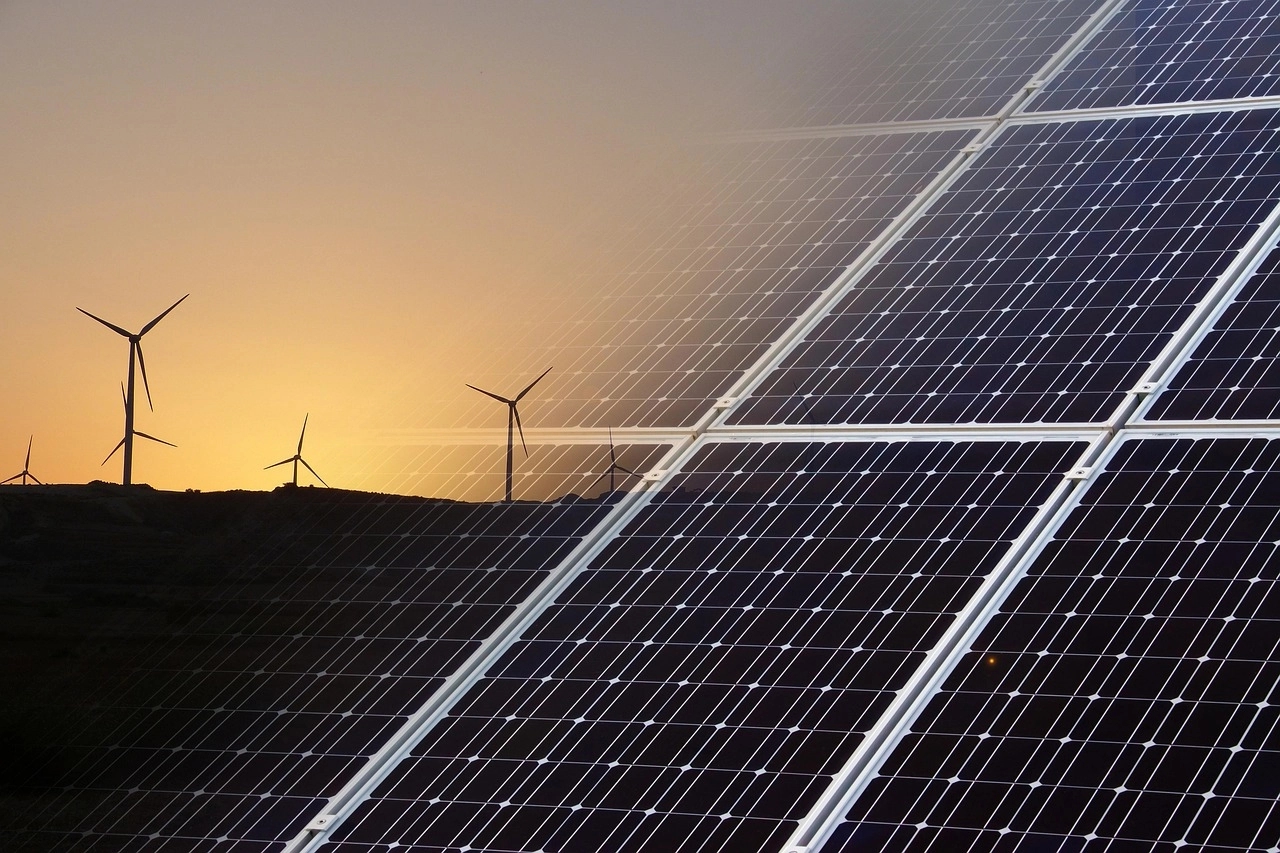 Kombination aus Nahaufnahme von Solarmodulen und Windkraftanlagen als Silhouetten vor einem goldenen Sonnenuntergang.