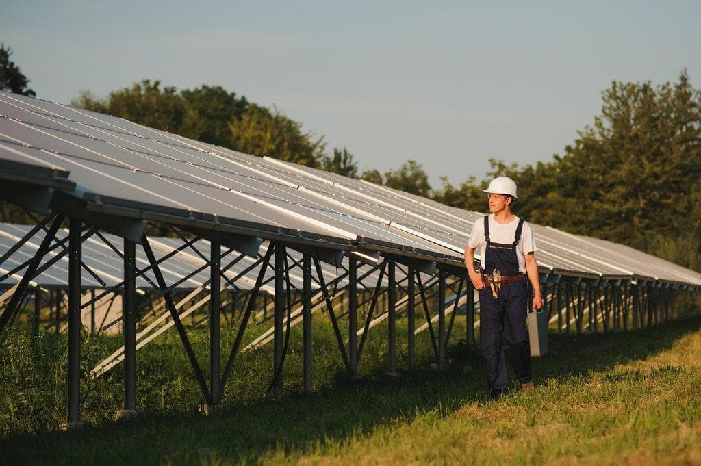 Männlicher Ingenieur mit Helm steht neben Solarpanels
